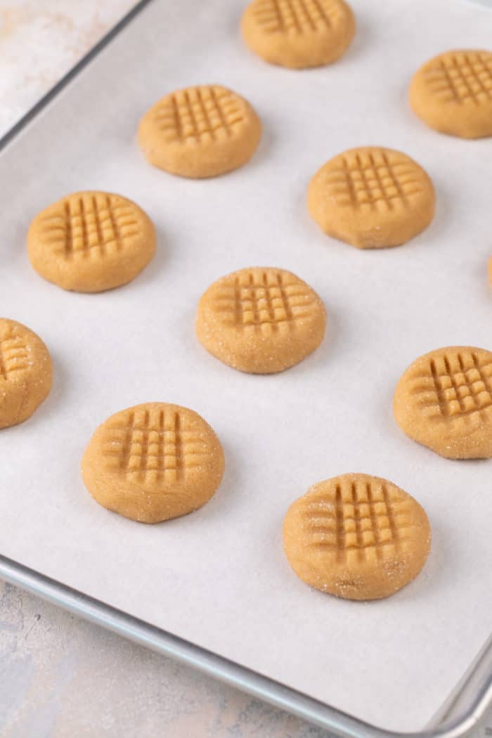 Honey peanut butter cookie dough flatted with a fork on a parchment-lined baking sheet.