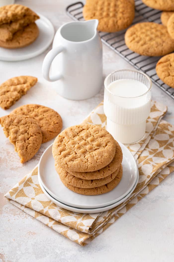 Plate with 4 honey peanut butter cookies on it with more cookies and a glass of milk in the background.