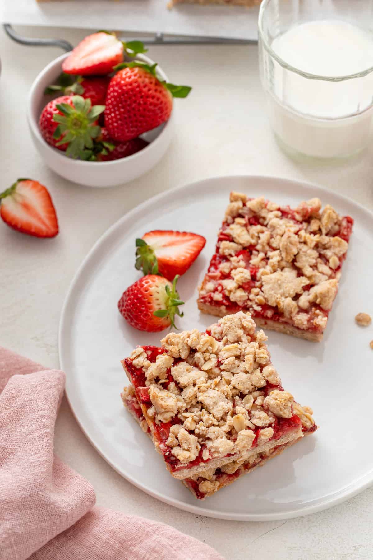 Strawberry oatmeal bars arranged next to fresh strawberries on a white plate.