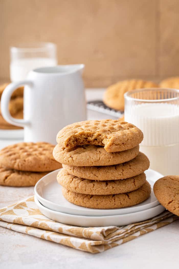 5 peanut butter cookies stacked on a white plate. A bite has been taken from the top cookie.