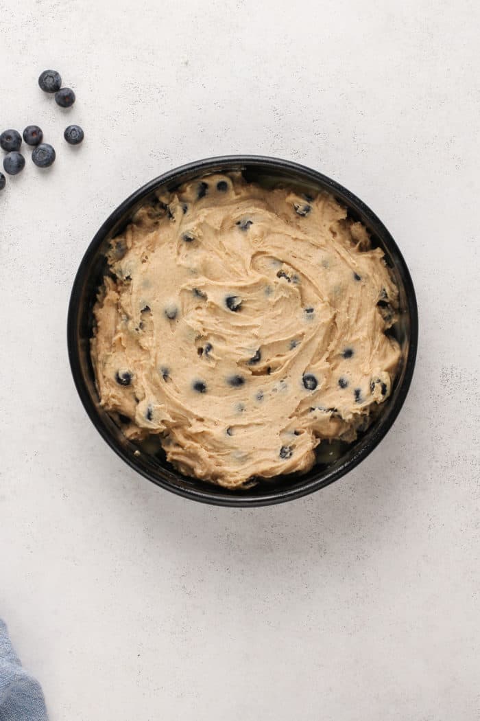 Blueberry buckle batter spread into a cake pan.