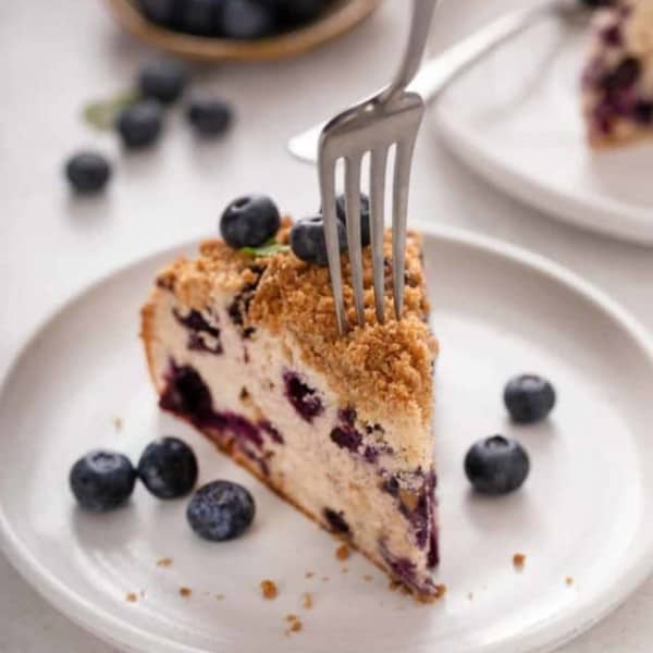 Fork about to take a bite from a slice of blueberry buckle on a white plate.