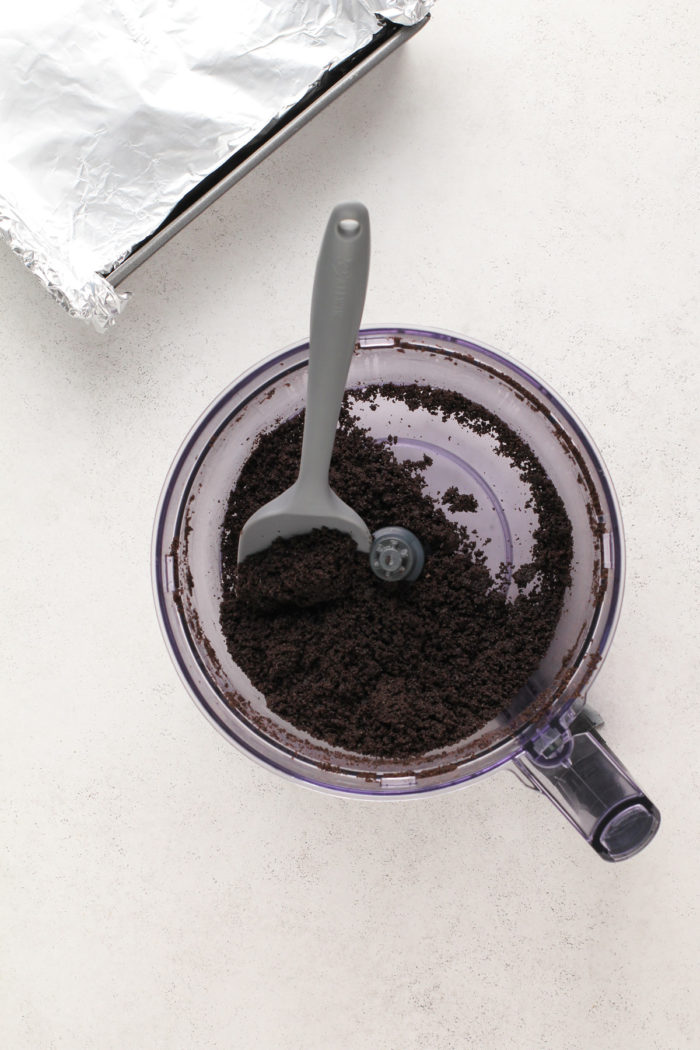 Crushed oreo cookies in the bowl of a food processor.