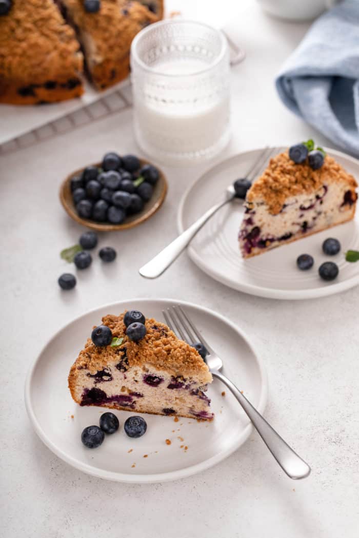 Two white plates, each with a slice of blueberry buckle on them.