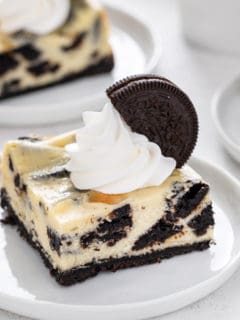 Oreo cheesecake bar topped with whipped cream on a white plate.
