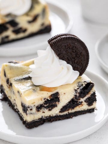 Oreo cheesecake bar topped with whipped cream on a white plate.