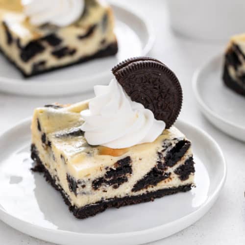 Oreo cheesecake bar topped with whipped cream on a white plate.