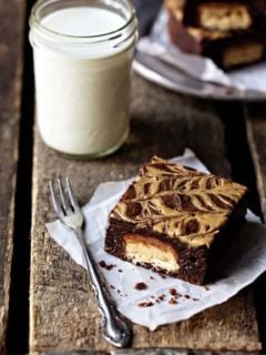 A peanut butter brownie next to a fork and glass of milk on a wooden table