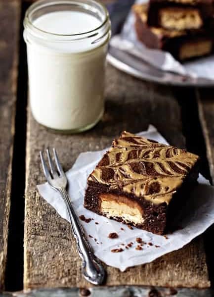 A peanut butter brownie next to a fork and glass of milk on a wooden table