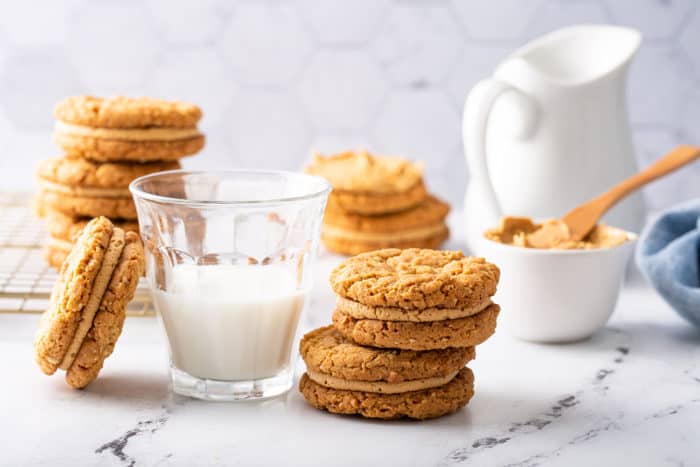 Biscoff sandwich cookies stacked next to a glass of milk on a marble counter