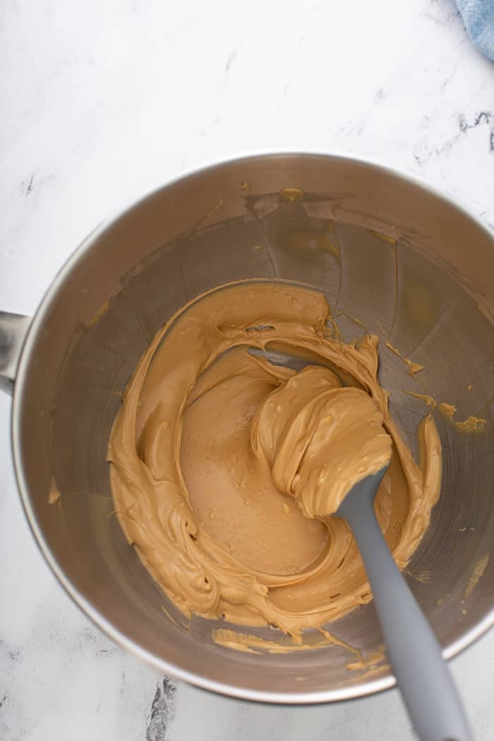 Spatula stirring creamed biscoff spread and butter in a metal mixing bowl