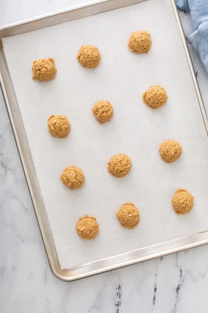 Portioned biscoff cookie dough lined up on a parchment-lined baking sheet