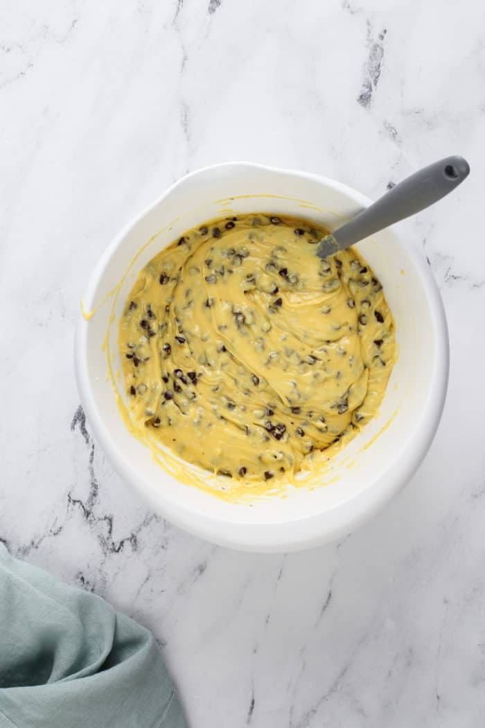 Chocolate chip bundt cake batter in a white mixing bowl on a marble countertop.