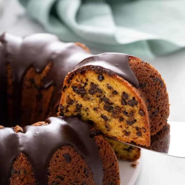 Cake server lifting up a slice of chocolate chip bundt cake from the whole cake.