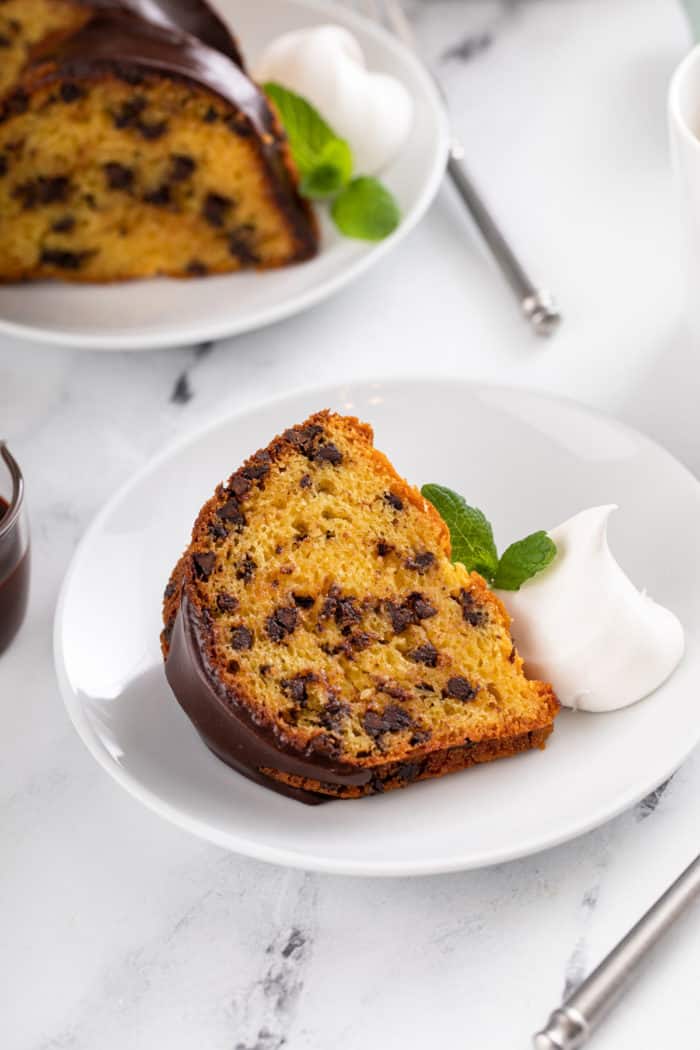 Slice of chocolate chip bundt cake next to a dollop of whipped cream on a white plate.