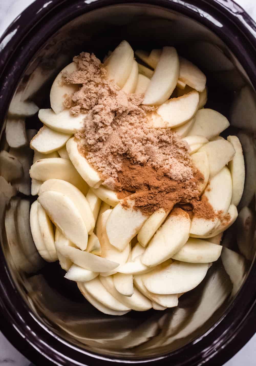 Sliced apples, brown sugar and apple pie spice in a slow cooker crock