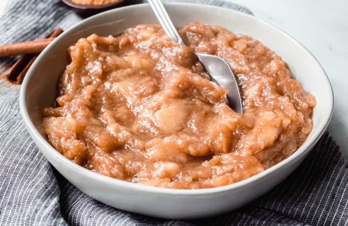 Homemade crockpot applesauce in a white bowl with a spoon in it