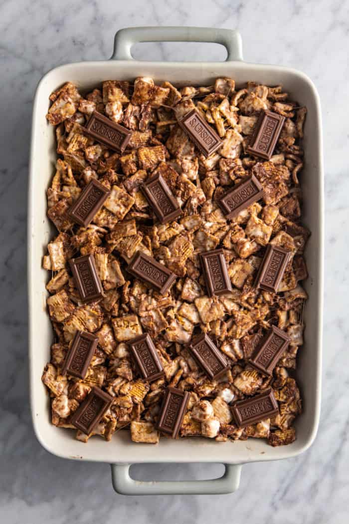 Assembled golden graham s'mores, decorated with pieces of a hershey's bar, in a white baking dish.