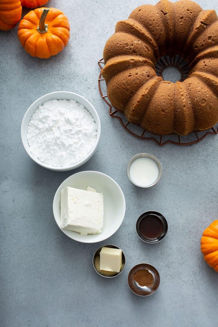 Cream cheese frosting ingredients next to a pumpkin bundt cake on a gray counter