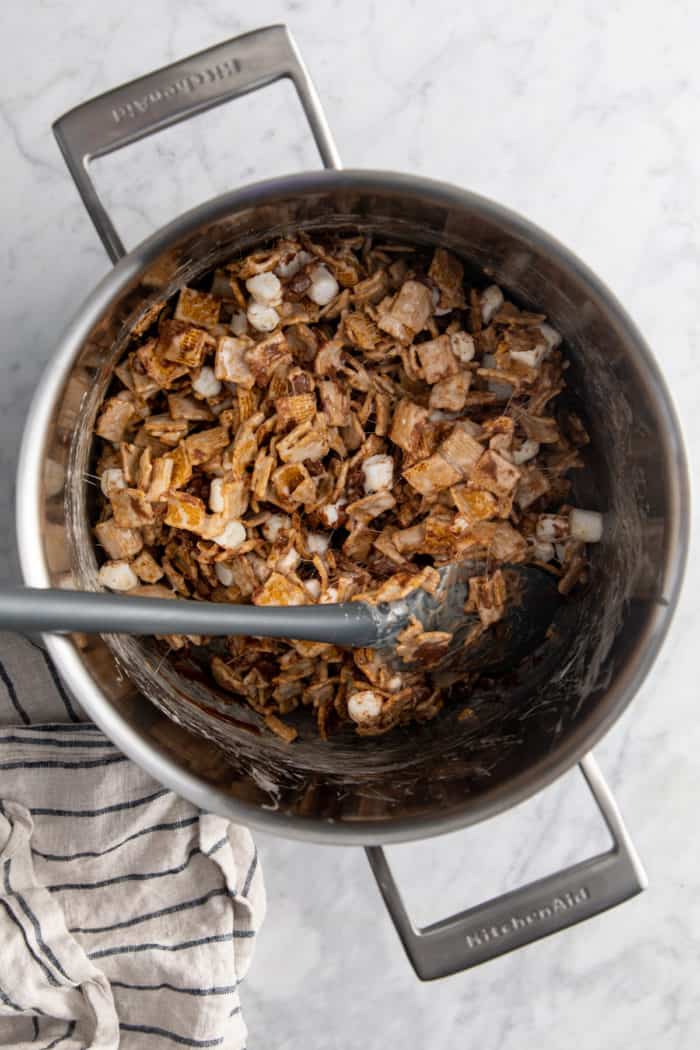 Spatula mixing together golden graham s'mores in a metal saucepan.