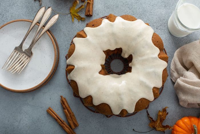 Overhead view of a frosted pumpkin bundt cake next to white plates and forks for serving