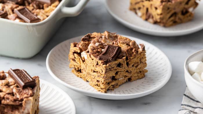 Golden graham s'more on a white plate, surrounded by more plates and a baking dish of s'mores bars.