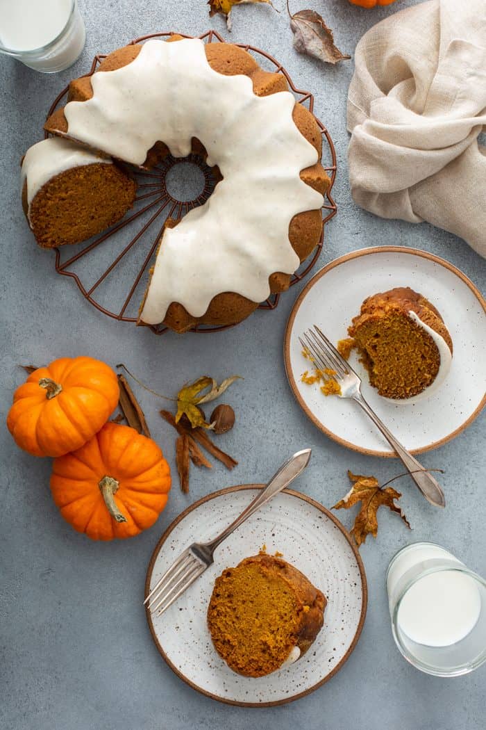 Overhead view of a sliced pumpkin bundt cake next to two white plates with slices of cake and forks on them