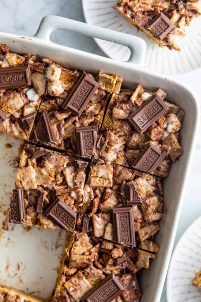 Close up of sliced golden graham s'mores in a white baking dish, with some of the bars removed.