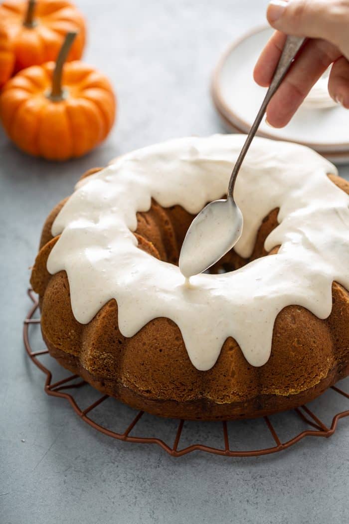 Spoon drizzling cream cheese frosting onto a pumpkin bundt cake