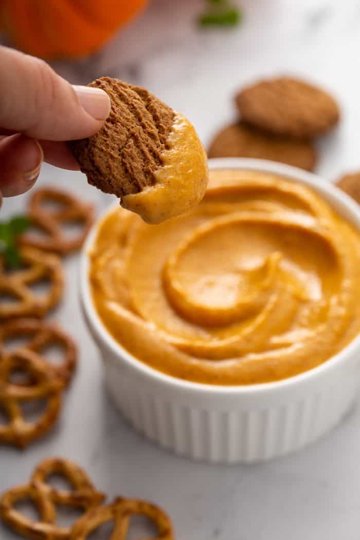 Hand dipping a gingersnap cookie into a bowl of pumpkin dip