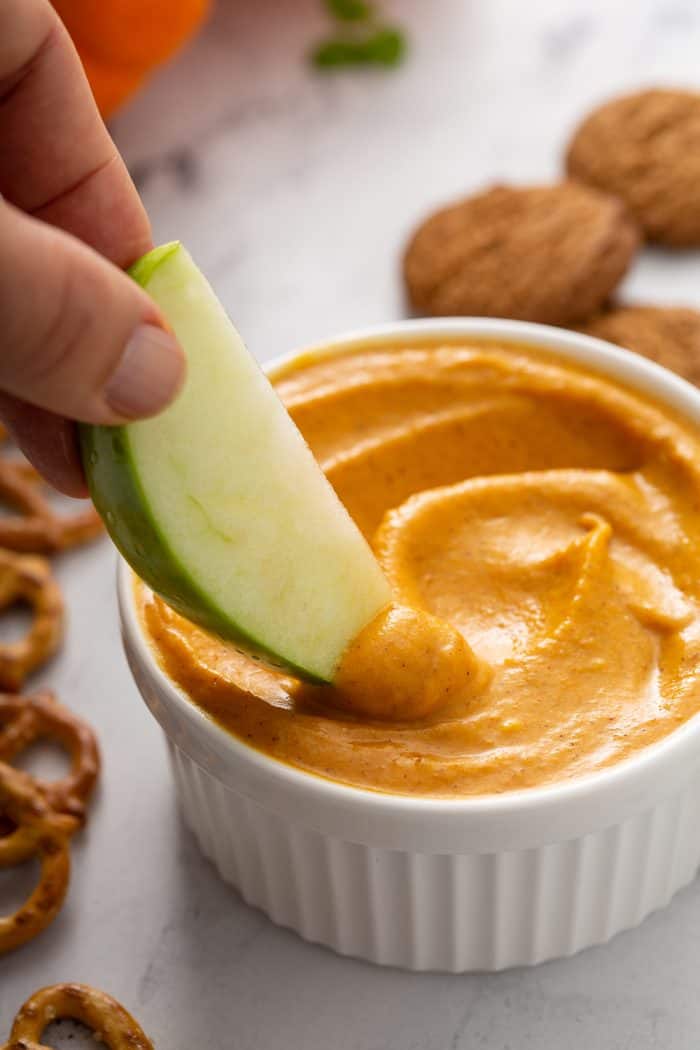 Hand dipping an apple slice into a bowl of pumpkin dip