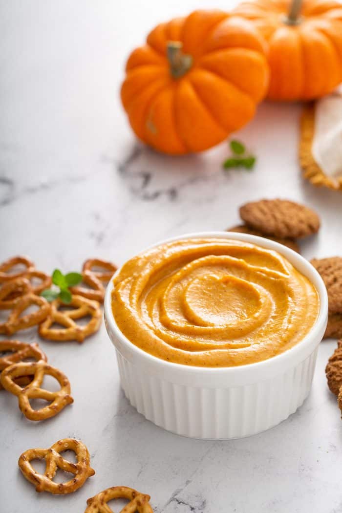 Bowl of pumpkin dip on a marble counter surrounded by pretzels