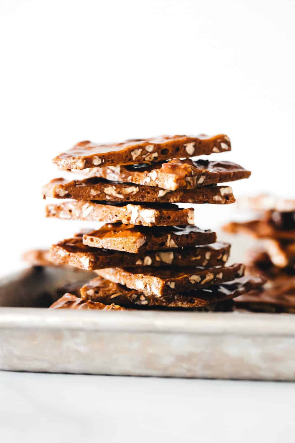 Shards of pecan brittle stacked on a metal sheet tray