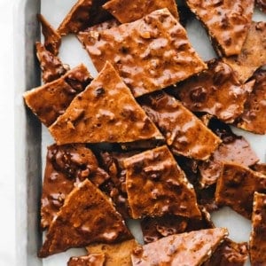 Pieces of pecan brittle scattered on parchment paper on a sheet tray