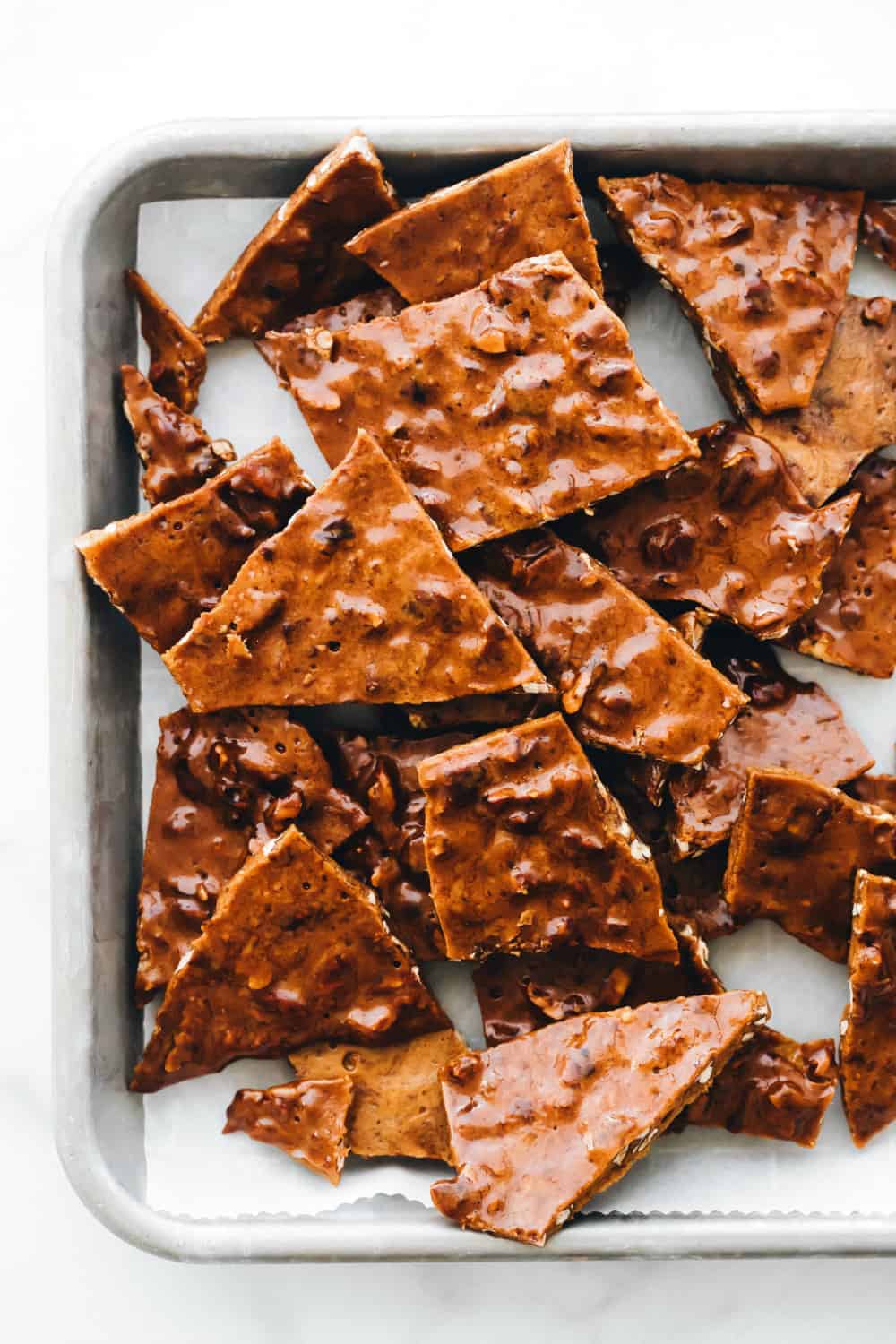 Pieces of pecan brittle scattered on parchment paper on a sheet tray