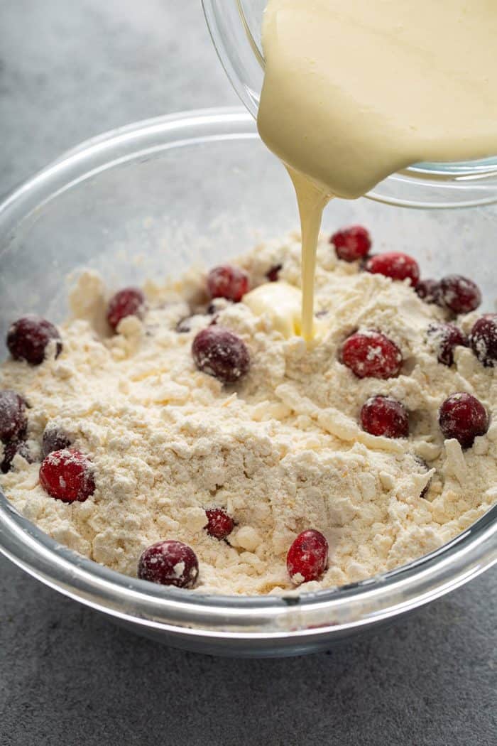 Wet ingredients being poured into a glass mixing bowl holding the dry ingredients for cranberry scones