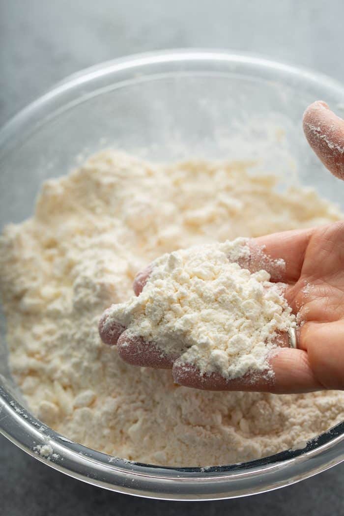 Hand showing the crumbly texture of butter mixed into the dry ingredients for scones