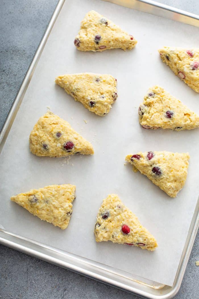 Cut cranberry orange scones arranged on a parchment-lined baking sheet, ready to be baked