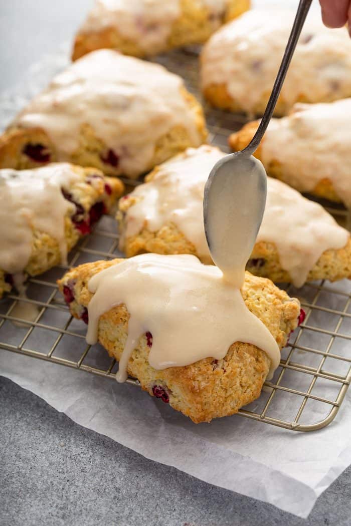 Spoon spooning glaze on top of cranberry orange scones on a wire rack