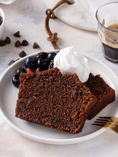 Slice of chocolate bread topped with whipped cream and fresh berries on a white plate.