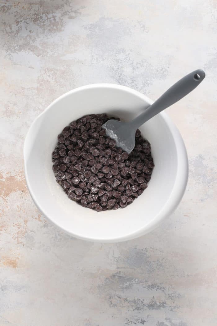 Chocolate chips tossed with flour in a white mixing bowl.