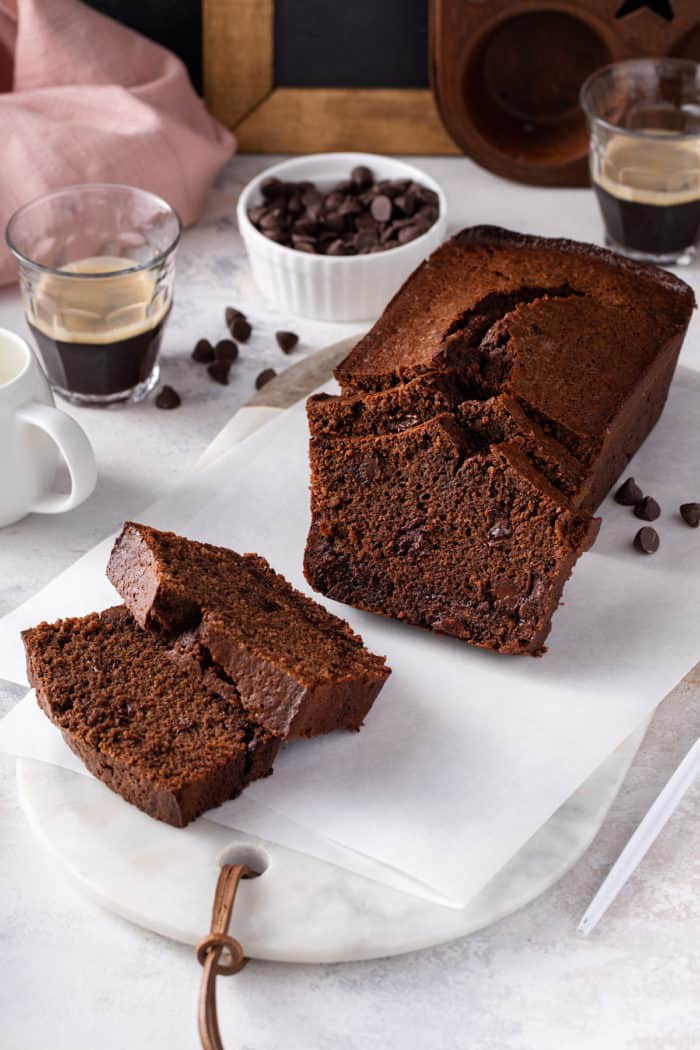 Loaf of chocolate bread set on a white board with several slices cut from it.