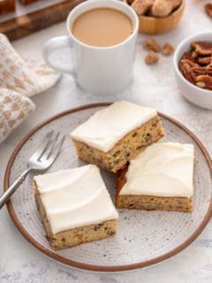 Three pieces of frosted banana bars arranged next to a fork on a stoneware plate.
