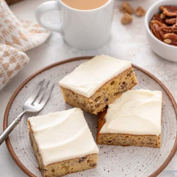 Three pieces of frosted banana bars arranged next to a fork on a stoneware plate.