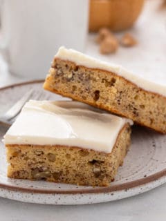 Two banana bars topped with cream cheese frosting on a stoneware plate.