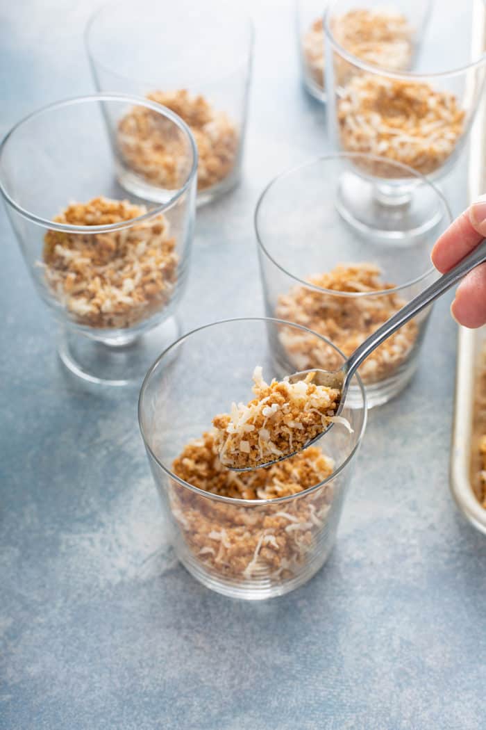 Spoon portioning graham cracker crumble into individual glass dishes