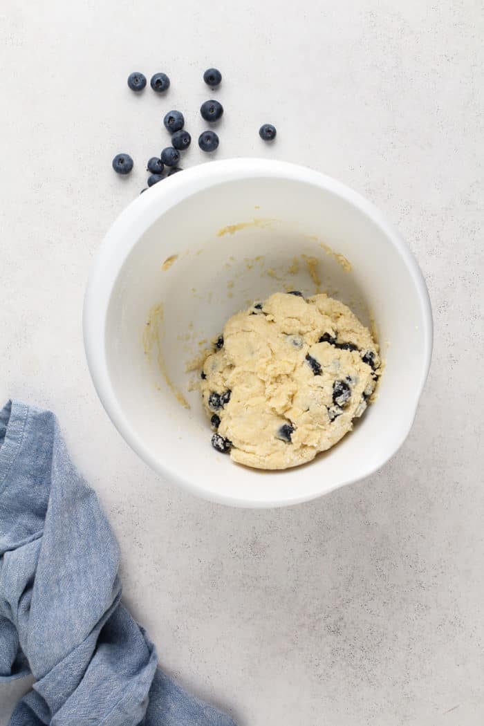 Blueberry scone dough formed into a ball in a white mixing bowl.