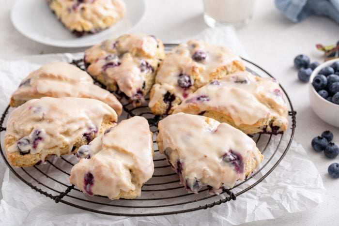 Round wire cooling rack holding glazed blueberry scones.