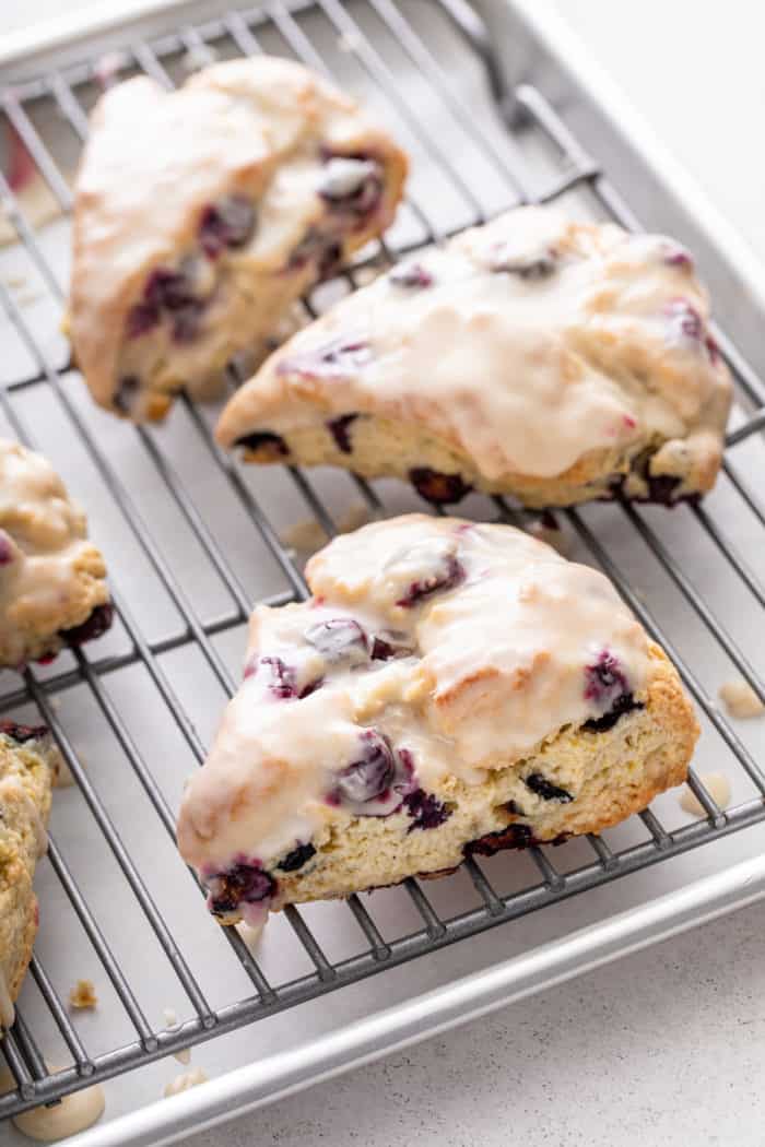 Glazed blueberry scones set on a wire cooling rack over a sheet pan.