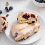 Two blueberry scones on a white plate. One of them is broken in half.